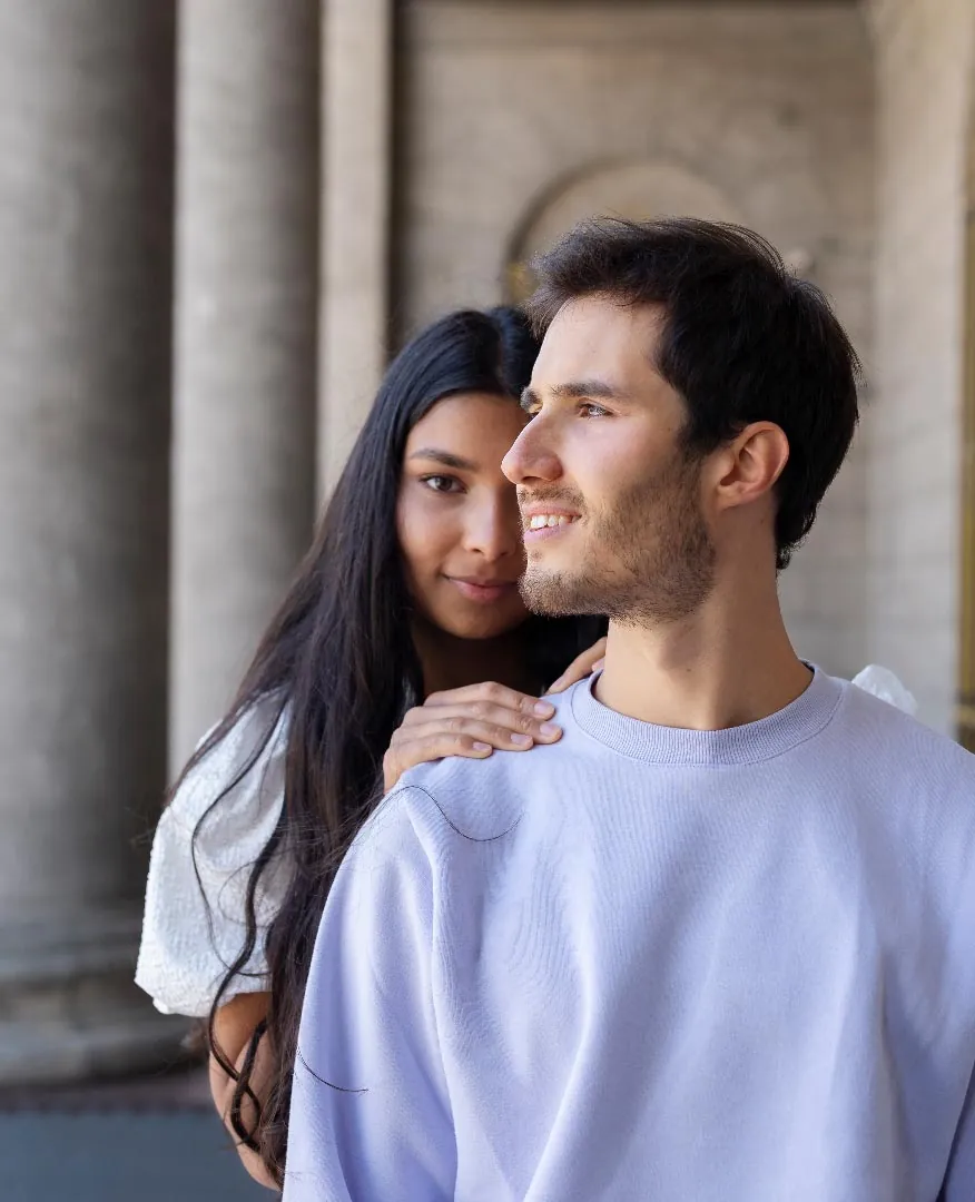 Un jeune couple souriant, elle pose les mains sur les épaules de son compagnon