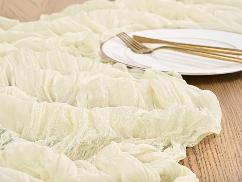 Chemin de table en gaze de coton beige froissé sous une assiette et des couverts dorés