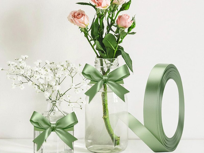 Rouleau de ruban satin vert sauge et nœud autour d’un vase de fleurs